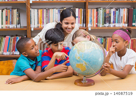 Cute pupils and teacher looking at globe in library Cute pupils and teacher looking at globe in library 14087519