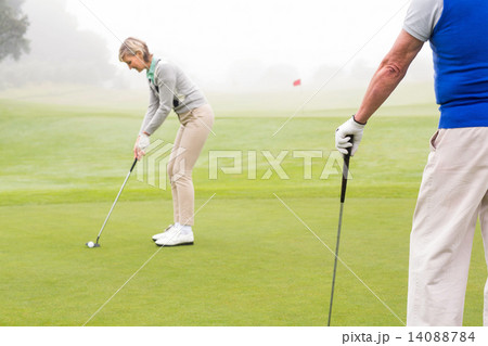 Lady golfer teeing off for the day watched by partner Lady golfer teeing off for the day watched by partner 14088784