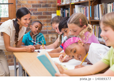 Pretty teacher helping pupils in library Pretty teacher helping pupils in library 14089377