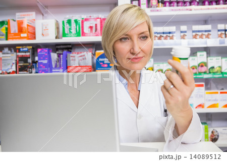 Smiling pharmacist looking at medicine 14089512
