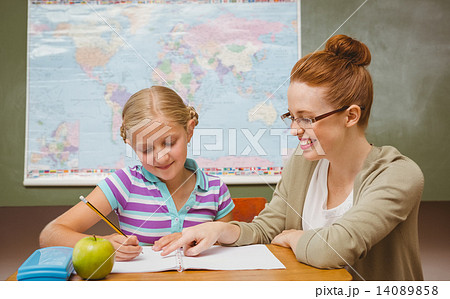 Teacher assisting girl with homework in classroom 14089858