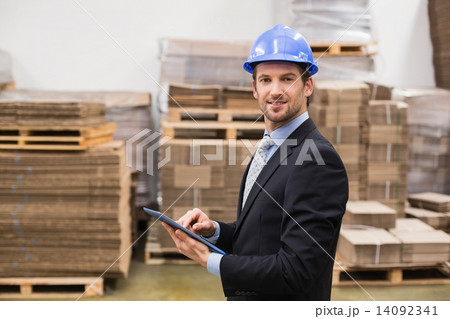 Warehouse manager wearing hard hat using tablet Warehouse manager wearing hard hat using tablet 14092341