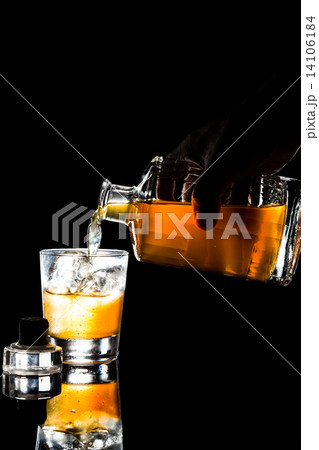 Hand holding and pouring whiskey onto a glass with ice in dark background 14106184