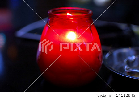 Burning candle in red glass holder and metal ashtray 14112945
