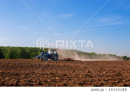 Blue tractor plowing field in spring Blue tractor plowing field in spring 14143189