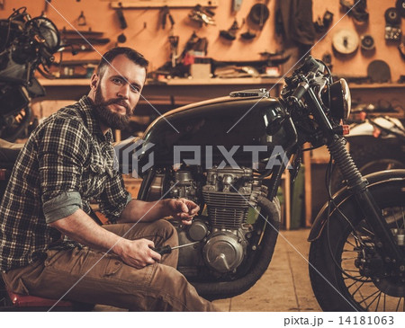 Mechanic building vintage style cafe-racer motorcycle in custom garage Mechanic building vintage style cafe-racer motorcycle in custom garage 14181063