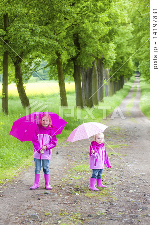 little girls wearing rubber boots with umbrellas in spring alley 14197831