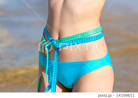 Young woman measuring waist with two tapes measure on the beach Young woman measuring waist with two tapes measure on the beach 14199651