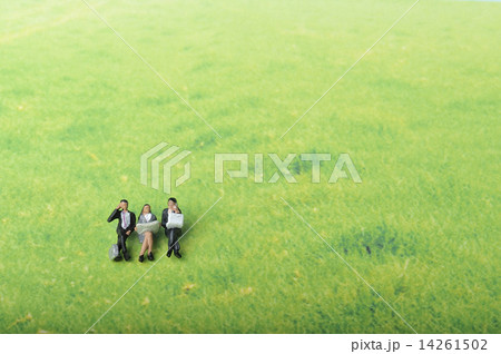 広い草原の中で座って仕事をしている3人のビジネスマンの写真素材