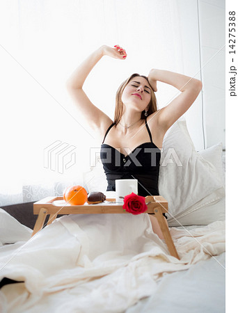 Beautiful woman sitting in bed and stretching while having break Beautiful woman sitting in bed and stretching while having break 14275388