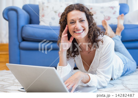 Smiling woman lying on the floor and using her laptop Smiling woman lying on the floor and using her laptop 14282487