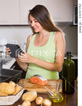 Woman cooking salmon with ereader Woman cooking salmon with ereader 14297762