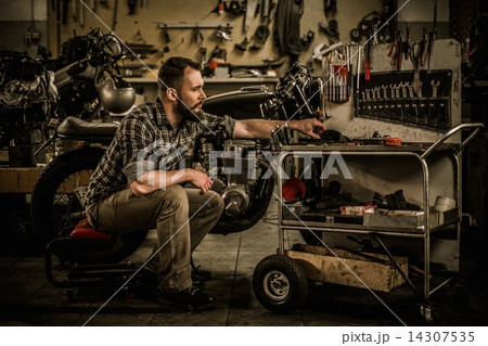 Mechanic building vintage style cafe-racer motorcycle  in custom garage 14307535