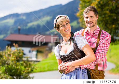 Couple in Tracht standing on meadow in alp mountains 14357576
