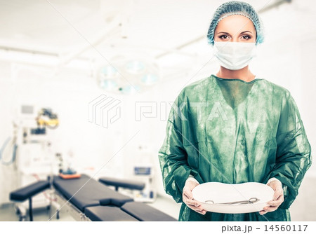 Young woman doctor in cap and face mask holding medicine tray with surgery tools 14560117