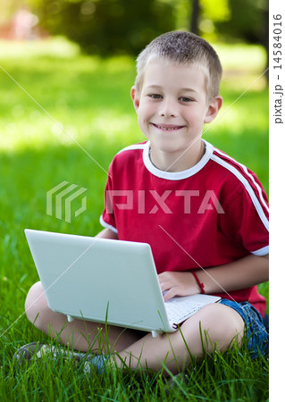 boy sitting with a laptop on the grass boy sitting with a laptop on the grass 14584016