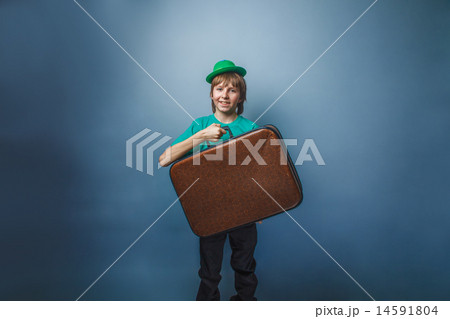 European-looking boy of ten years in a hat holding a suitcase in hand, itinerary on a blue backgroun 14591804