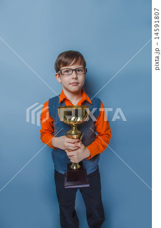 European-looking boy of ten years in glasses holding a cup, award joy on a blue background European-looking boy of ten years in glasses holding a cup, award joy on a blue background 14591807