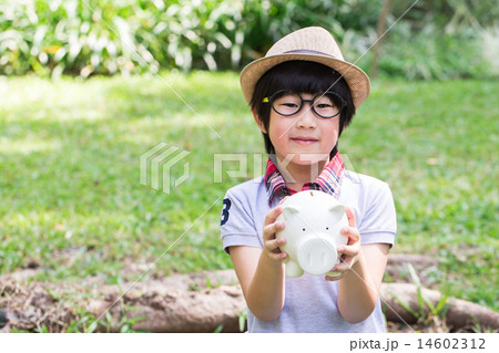 Little asian boy is holding his piggy bank in park Little asian boy is holding his piggy bank in park 14602312