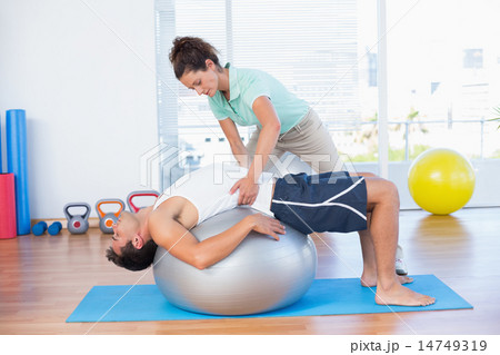 Trainer helping man with exercise ball Trainer helping man with exercise ball 14749319