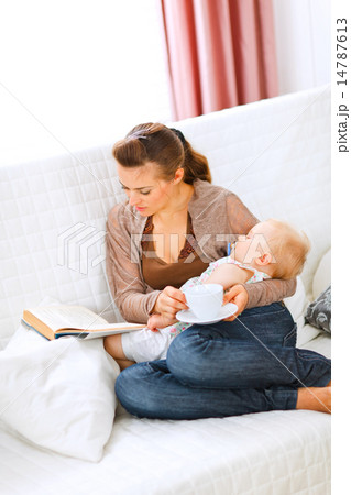 Young mom resting while baby sleep by having tea and reading boo 14787613