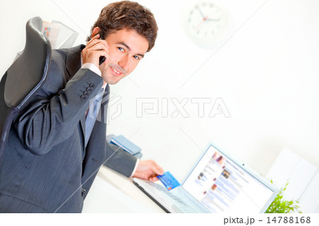 Smiling businessman in office making purchase by phone and credit card. 14788168