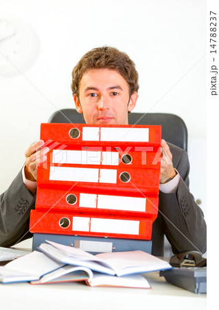 Sitting at office desk confused businessman looking out from pil Sitting at office desk confused businessman looking out from pil 14788237