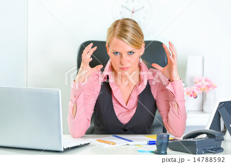 Angry business woman sitting at office desk and holding hands near head. 14788592