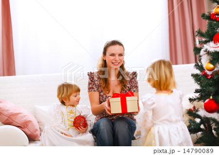 Two twins girl presenting gift to mother near Christmas tree 14790089