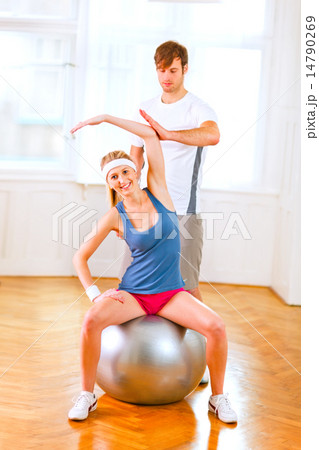 Smiling girl making exercises on fitness ball assisted by her pe 14790269