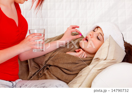 Girl giving pill and cup of water to her ill girlfriend 14790732