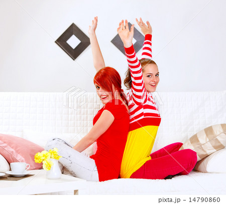 Two beautiful girlfriends sitting on sofa back to back and rejoi 14790860