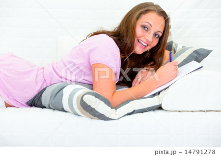 Pleased pretty woman lying on couch and writing in diary. 14791278
