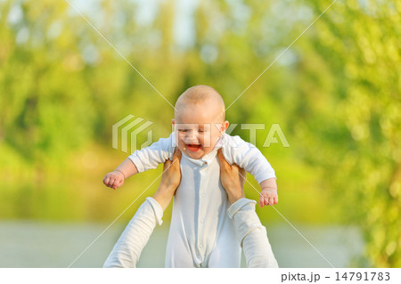 Mother's hands holding laughing baby against sunny leaves. Baby looking on mother.. Mother's hands holding laughing baby against sunny leaves. Baby looking on mother.. 14791783