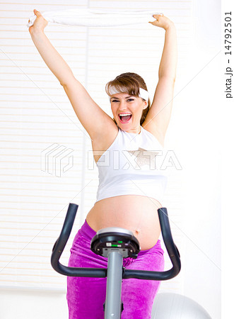 Happy beautiful pregnant woman working out on stationary bicycle. 14792501