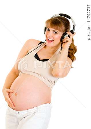 Smiling pregnant woman holding her belly and listening music in headphones . Smiling pregnant woman holding her belly and listening music in headphones . 14792737