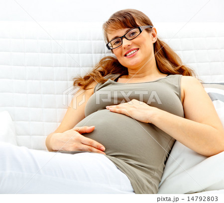 Smiling beautiful pregnant woman lying on couch and holding her belly.. Smiling beautiful pregnant woman lying on couch and holding her belly.. 14792803