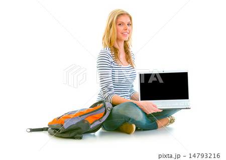Smiling teen girl sitting on floor and showing laptops blank scr 14793216
