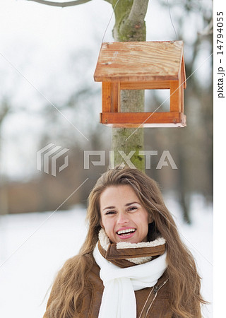 Portrait of smiling young woman standing under bird feeder in wi Portrait of smiling young woman standing under bird feeder in wi 14794055