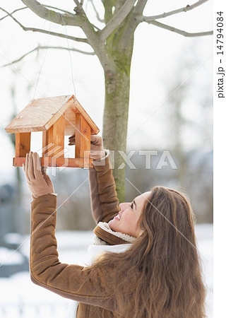 Happy young woman adding meal into bird feeder 14794084