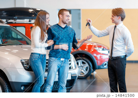 Sales consultant gives keys from new car to young couple Sales consultant gives keys from new car to young couple 14841500