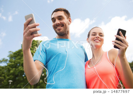 two smiling people with smartphones outdoors 14877697