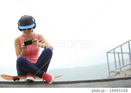 woman skateboarder listening music from cellphone woman skateboarder listening music from cellphone 14893188
