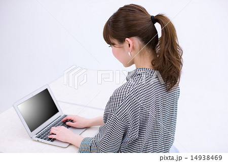 ノートパソコンを操作する若い女性の後ろ姿の写真素材