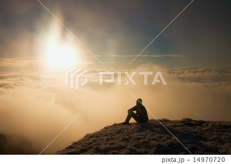 Tired hiker in black sit on frozen grass on hill Tired hiker in black sit on frozen grass on hill 14970720