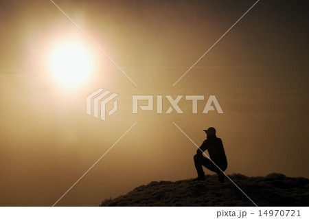 Tired hiker in black sit on frozen grass on hill Tired hiker in black sit on frozen grass on hill 14970721