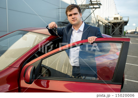 handsome man in suit leaning against new car and showing keys 15020006