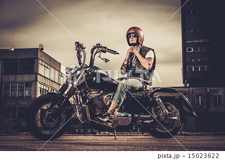 Tattooed biker and his bobber style motorcycle on a city streets Tattooed biker and his bobber style motorcycle on a city streets 15023622