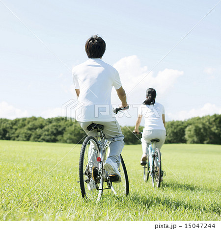 草原で自転車に乗るカップルの後姿の写真素材