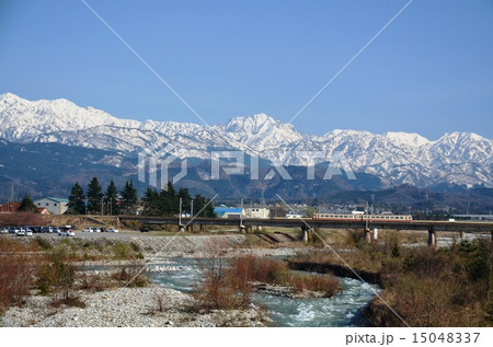 雪の北アルプスを背景に走る地鉄電車 15048337